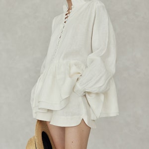 May include: A white linen button-up shirt with a ruffled hem and a straw hat.