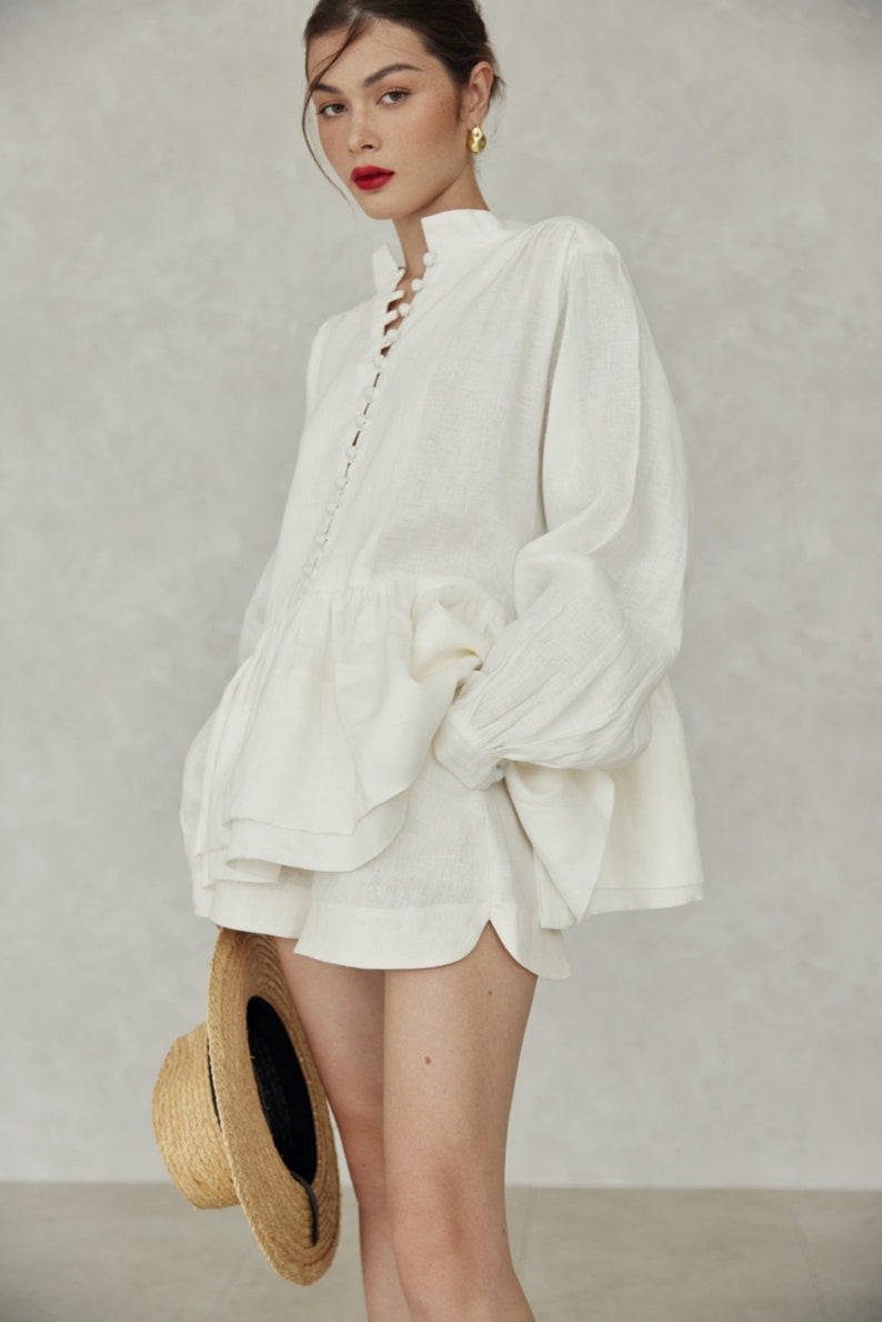 May include: A white linen button-up shirt with a ruffled hem and a straw hat.