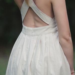 May include: A white linen dress with a criss-cross back design and a pleated skirt.