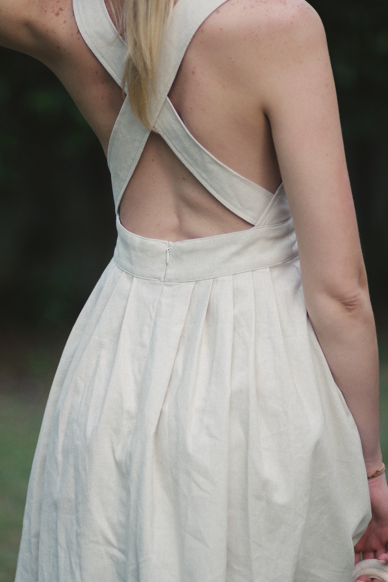 May include: A white linen dress with a criss-cross back design and a pleated skirt.