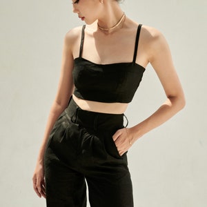 K&ouml;nnte beinhalten: Ein schwarzes Crop-Top und eine passende weite Hose. Das Top hat einen quadratischen Ausschnitt und d&uuml;nne Tr&auml;ger. Die Hose hat eine hohe Taille und einen G&uuml;rtel.