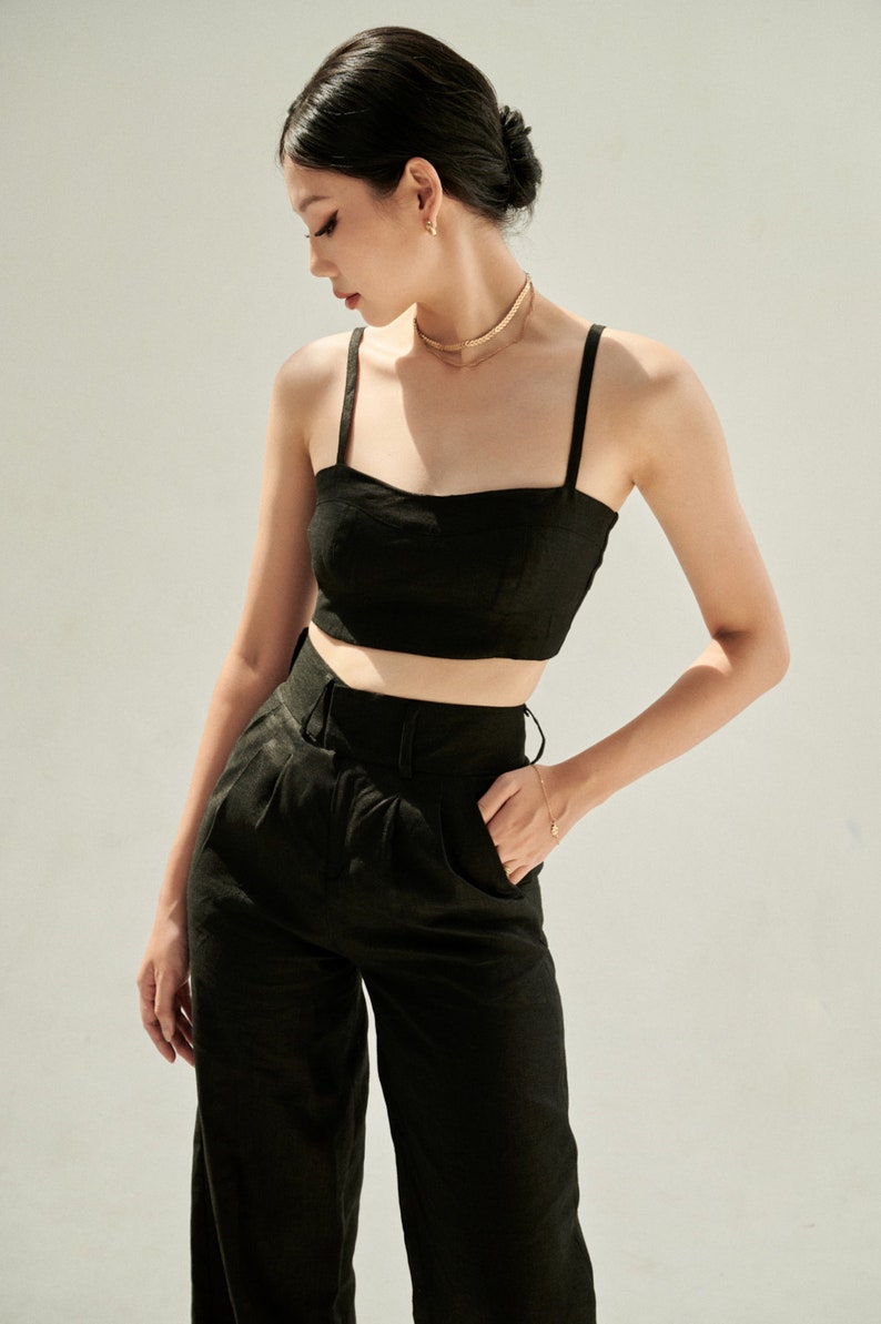 K&ouml;nnte beinhalten: Ein schwarzes Crop-Top und eine passende weite Hose. Das Top hat einen quadratischen Ausschnitt und d&uuml;nne Tr&auml;ger. Die Hose hat eine hohe Taille und einen G&uuml;rtel.