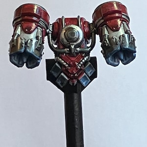 May include: A red and silver robot arm with a black base. The arm has a large, round, silver eye in the centre and is attached to a black base.