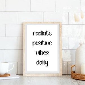 Puede incluir: Un cartel enmarcado con las palabras "radiate positive vibes daily" en escritura negra. El marco es de madera clara y la impresión se muestra sobre un fondo blanco. La imagen está colocada contra una pared de azulejos blancos.