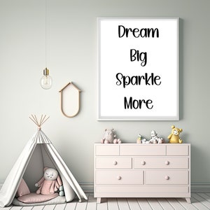 K&ouml;nnte beinhalten: Ein gerahmter Druck mit den Worten "Dream Big Sparkle More" in schwarzer Schrift h&auml;ngt &uuml;ber einer rosa Kommode. Ein wei&szlig;es Tipi mit einem Pl&uuml;schtier und eine goldene Leuchte befinden sich ebenfalls im Raum. Der Raum hat eine helle, luftige Atmosph&auml;re.