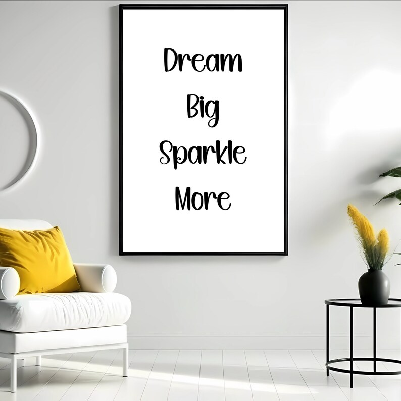K&ouml;nnte beinhalten: Gerahmter Druck mit den Worten "Dream Big Sparkle More" in schwarzer Schrift auf wei&szlig;em Hintergrund. Der Rahmen ist schwarz. Der Druck h&auml;ngt an einer wei&szlig;en Wand, mit einem wei&szlig;en Stuhl und einem gelben Kissen im Vordergrund.