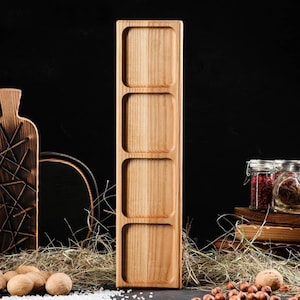 Puede incluir: Una bandeja de servir de madera con cuatro compartimentos cuadrados. La bandeja está hecha de madera marrón claro y tiene un acabado natural.