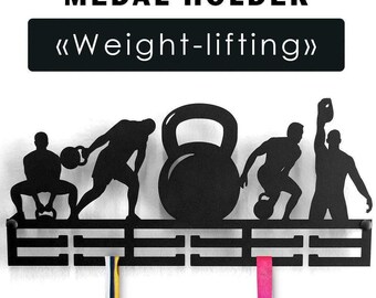 May include: A black metal medal holder featuring the text MEDAL HOLDER and Weight-lifting. The design includes silhouettes of individuals performing various weightlifting exercises with kettlebells, and two hanging ribbons.