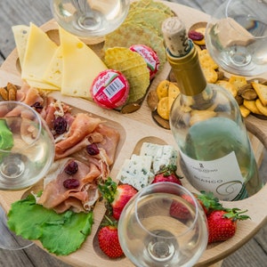 K&ouml;nnte beinhalten: Ein Holztablett mit vier Weingl&auml;sern, einer Flasche Wei&szlig;wein, K&auml;se, Crackern, Obst und Fleisch. Das Tablett ist so konzipiert, dass die Gl&auml;ser an ihrem Platz bleiben.