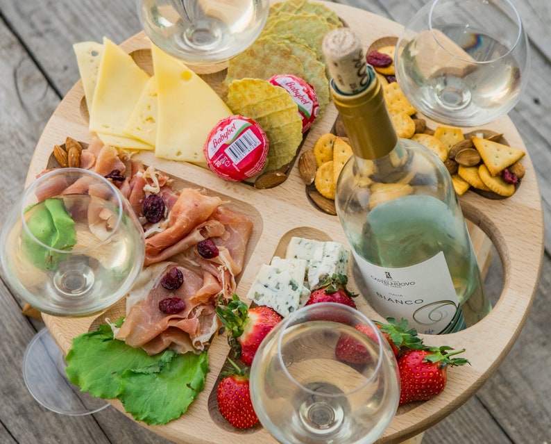 K&ouml;nnte beinhalten: Ein Holztablett mit vier Weingl&auml;sern, einer Flasche Wei&szlig;wein, K&auml;se, Crackern, Obst und Fleisch. Das Tablett ist so konzipiert, dass die Gl&auml;ser an ihrem Platz bleiben.
