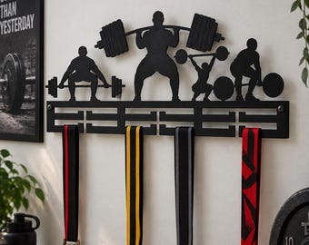 May include: A black metal wall-mounted medal hanger featuring silhouettes of four weightlifters in various lifting positions. The rack includes a horizontal bar with hooks to display four hanging medals with red, yellow, grey, and patterned ribbons.