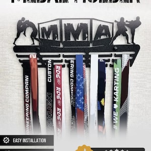 May include: A black metal medal holder featuring the text MEDAL HOLDER at the top and MMA in the centre. The design includes silhouettes of fighters on both sides and multiple horizontal slots for hanging medals with various colourful ribbons attached.