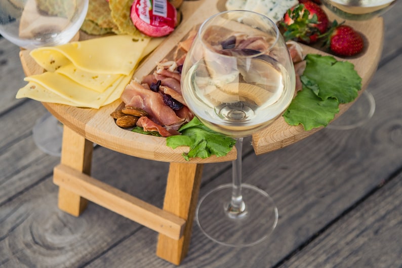 K&ouml;nnte beinhalten: Ein Holztablett mit eingebautem St&auml;nder, gef&uuml;llt mit K&auml;se, Crackern, Prosciutto, Mandeln und Erdbeeren. Ein Glas Wei&szlig;wein steht auf dem Tablett.