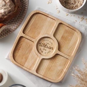 Könnte beinhalten: Ein quadratisches Serviertablett aus hellem Holz mit vier unterteilten Abschnitten und einem runden Fach in der Mitte. Die Mitte ist mit dem Text "Love you. Wilson 2018 Noah & Lisa" sowie Sternen und Punkten in dunkelbrauner Schrift graviert.