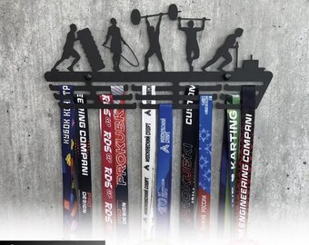May include: A black metal medal holder featuring silhouettes of athletes performing various sports activities. The top section displays the text MEDAL HOLDER. Below the figures are multiple horizontal bars designed to hang several colorful ribbons.