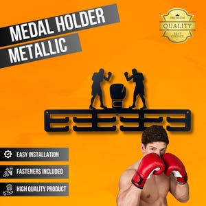 May include: Black metallic medal holder with a boxing theme. The holder features a silhouette of two boxers and a boxing glove. The text "MEDAL HOLDER METALLIC" is displayed at the top. The holder has multiple slots for medals.