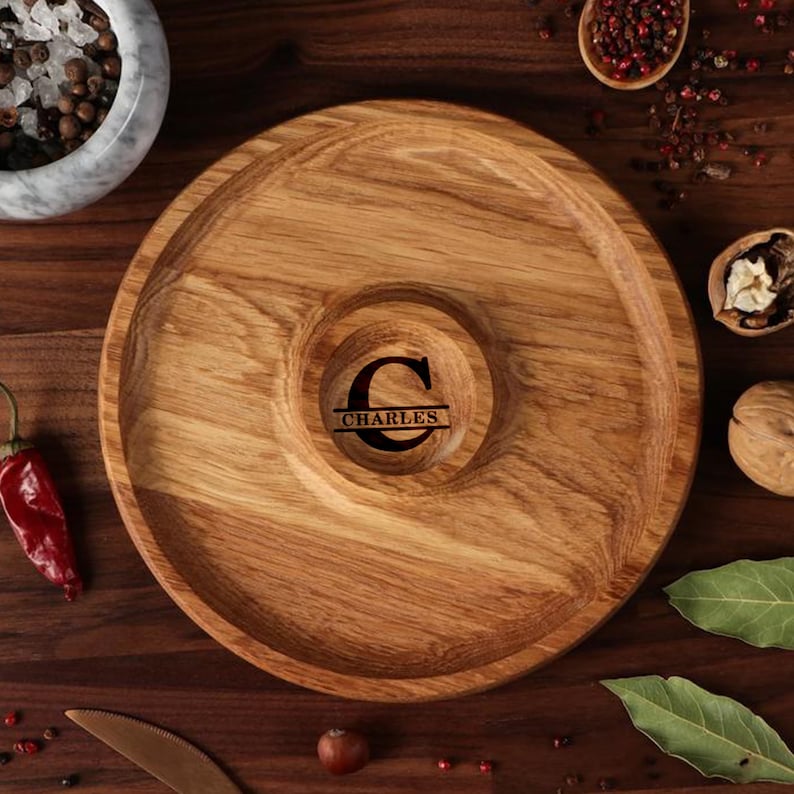 May include: A round wooden serving tray with a center dip. The tray is made of light brown wood and has a dark brown initial "C" with the name "CHARLES" engraved below it.