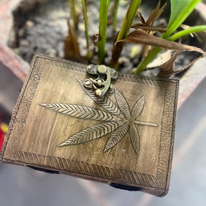 May include: A brown leather journal with a brass clasp and a leaf design embossed on the cover.