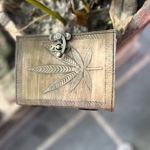 May include: A brown leather journal with a brass clasp and a carved marijuana leaf design.