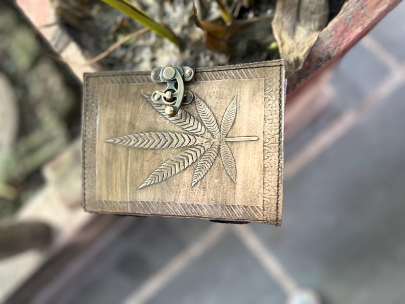 May include: A brown leather journal with a brass clasp and a carved marijuana leaf design.