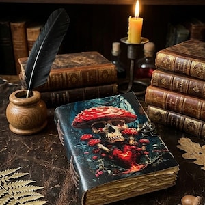 May include: A detailed image of a vintage-style journal with a mushroom and skull design. The journal is open on a leather surface, with a quill pen and inkwell, a lit candle, and stacks of old books in the background. Acorns and a fern are also present.