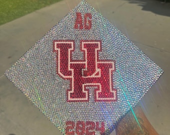 May include: A silver graduation cap decorated with rhinestones and a red and white University of Houston logo. The year 2023 is also displayed on the cap.