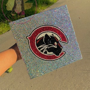 May include: A graduation cap covered in iridescent rhinestones with a red, white, and black Chicago Cubs logo.