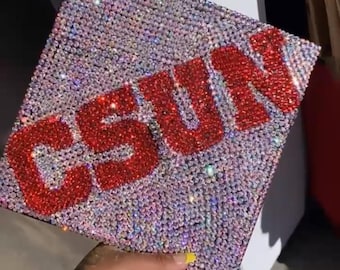 May include: A graduation cap covered in sparkling rhinestones with the letters "CSUN" in red rhinestones.