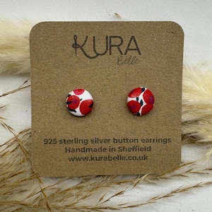 May include: A pair of 925 sterling silver button earrings with a red and white floral pattern. The earrings are handmade in Sheffield, England. The card reads "Kura Belle" and "www.kurabelle.co.uk".