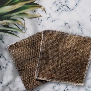 May include: Two brown burlap cleaning cloths with white stitching on a white marble surface.