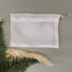 May include: White mesh laundry bag with a drawstring closure. The bag is made of a fine mesh material and is designed to hold delicate items during washing.