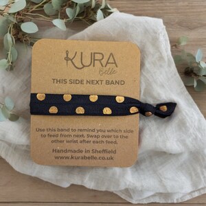 May include: A black elastic hair tie with gold polka dots and the text "KURA Belle THIS SIDE NEXT BAND" on a brown card. Use this band to remind you which side to feed from next. Swap over to the other wrist after each feed. Handmade in Sheffield www.kurabelle.co.uk