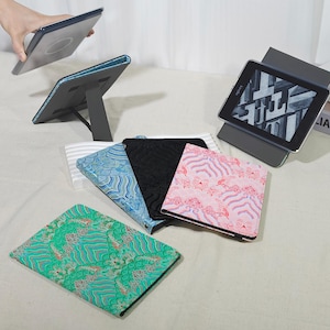 May include: Various patterned tablet cases in green, blue, black, and pink are displayed, with one case open and propped up. A tablet is shown in a case, and another case is being held up. The cases have a variety of designs.