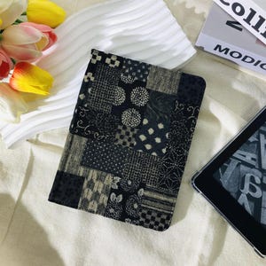 May include: A patchwork-style tablet cover in shades of black, gray, and beige. The cover features a variety of geometric and floral patterns. The cover is rectangular and appears to be made of fabric. A digital tablet is visible in the image.