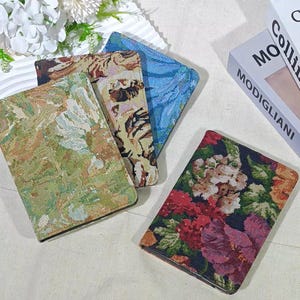 May include: A collection of tapestry-style book covers in various floral and abstract patterns. The covers feature a range of colors, including green, blue, and red, with intricate woven designs. The covers are rectangular and appear to be made of a textured fabric.