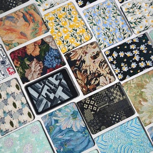 May include: A collection of various patterned cases, likely for electronic devices, arranged in a grid. The cases display diverse designs, including floral, abstract, and geometric patterns in a range of colors such as blue, yellow, and brown. The cases are rectangular and appear to be made of fabric.