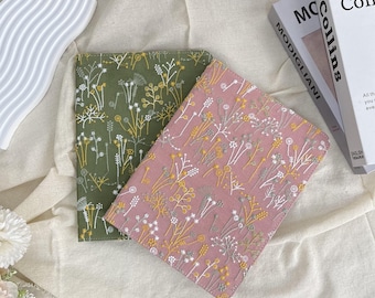 May include: Two embroidered journal covers. One is olive green, the other is dusty rose. Both feature a floral pattern in white, yellow, and gray thread. The covers are rectangular and appear to be made of fabric.