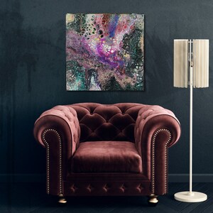 May include: Abstract painting with swirling colors of pink, purple, green, and black. The painting is hanging on a dark wall above a burgundy velvet armchair with a tall white lamp with a white shade.