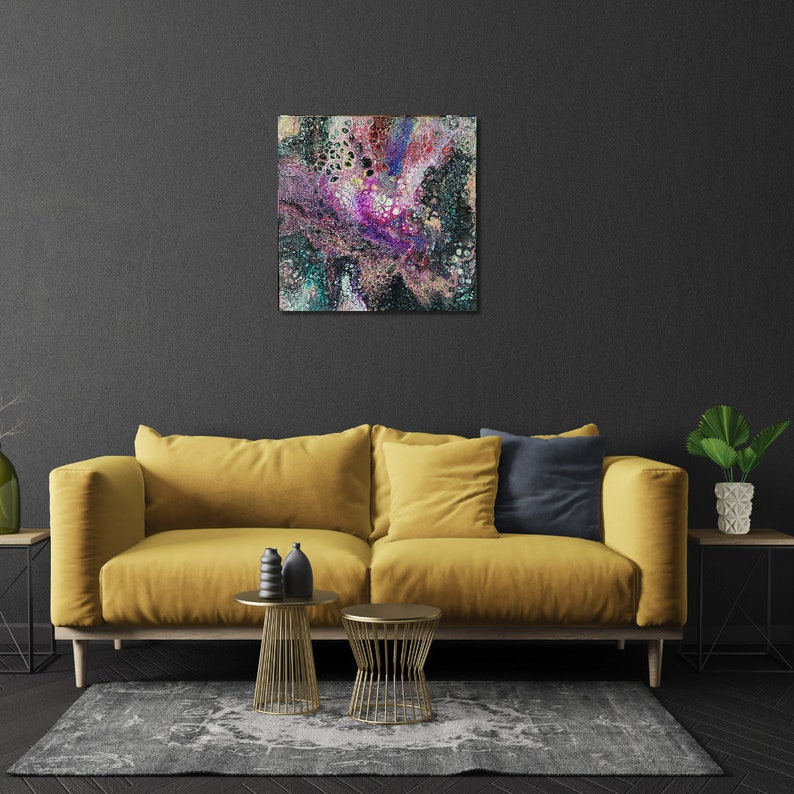 May include: Abstract painting with swirling colors of pink, purple, green, and black. The painting is framed and hanging on a dark gray wall above a yellow sofa.