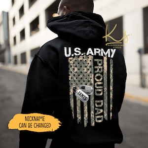 May include: Black hooded sweatshirt with a camouflage American flag design and the text "U.S. ARMY PROUD DAD" with a dog tag that says "JAMES". The text "NICKNAME CAN BE CHANGED" is on the bottom left corner of the sweatshirt.