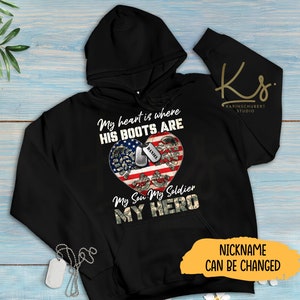 Peut inclure: Sweat-shirt à capuche noir avec un motif en forme de cœur représentant une paire de bottes militaires, un drapeau américain et une plaque d'identité avec le nom "Daniel". Le texte "My heart is where his boots are. My son, my soldier, my hero" est imprimé sur le sweat-shirt. Le texte "Nickname can be changed" est imprimé sous le motif.