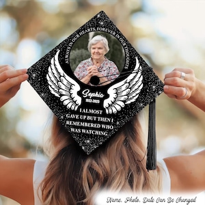 May include: A black graduation cap featuring a photo of a woman, angel wings, and the inscription "ALWAYS IN OUR HEARTS, FOREVER IN OUR THOUGHTS." The cap also includes the name "Sophia" and dates "1932-2025."