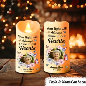 Puede incluir: Dos velas conmemorativas con una foto de una mujer y el texto "Your light will always shine in our Hearts". Las velas están decoradas con mariposas y flores. El texto "Jennifer 1946-2024" está impreso en la parte inferior de cada vela.