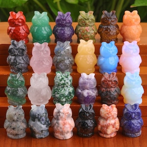 May include: A collection of 24 small owl figurines carved from various types of colorful gemstones. The owls are arranged in three rows of eight, with each owl facing forward. The owls are made of different types of gemstones, including amethyst, rose quartz, tiger's eye, and lapis lazuli.