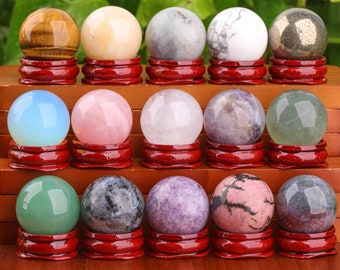 May include: A collection of 15 polished gemstone spheres displayed on small wooden stands. The spheres are arranged in three rows of five, with each sphere resting on a red stand. The spheres are made of various types of gemstones, including amethyst, rose quartz, tiger's eye, and aventurine.