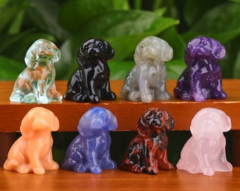 May include: Eight small, hand-carved dog figurines made of various semi-precious stones. The figurines are all in a sitting position and are arranged in a row on a wooden surface. The stones include clear quartz, black obsidian, grey labradorite, purple amethyst, orange carnelian, blue sodalite, red jasper, and pink rose quartz.