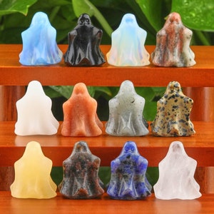 May include: A set of 12 ghost figurines carved from various types of polished stones, including clear, black, white, grey, brown, red, yellow, blue, and multi-coloured stones. The ghosts are arranged in three rows of four on a wooden shelf.