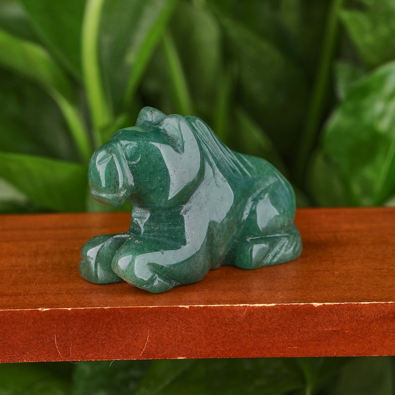 May include: A small, green jade carving of a lion, sitting on a wooden surface.