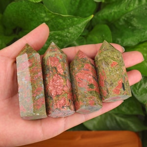 Puede incluir: Cuatro puntas de cristal de jaspe verde y rojo, también conocidas como hematoides, están dispuestas en fila sobre una mano. Las puntas están pulidas y tienen un aspecto natural y terroso.