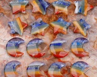 May include: A collection of 15 seven chakra stone carvings in the shapes of stars and crescent moons. The stones are layered with different colors, including red, orange, yellow, green, blue, indigo, and violet.